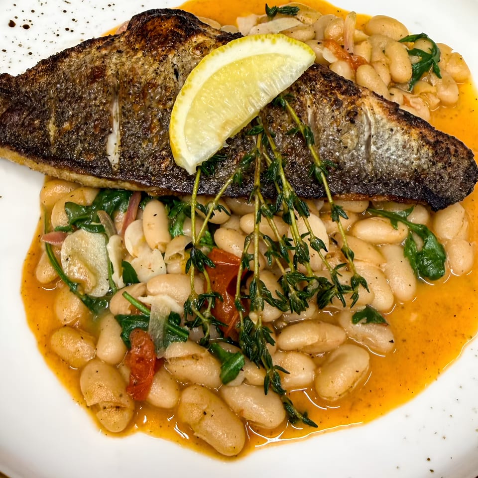 Crispy grilled fish fillet with lemon and thyme over white beans, spinach, and tomatoes in an orange sauce.