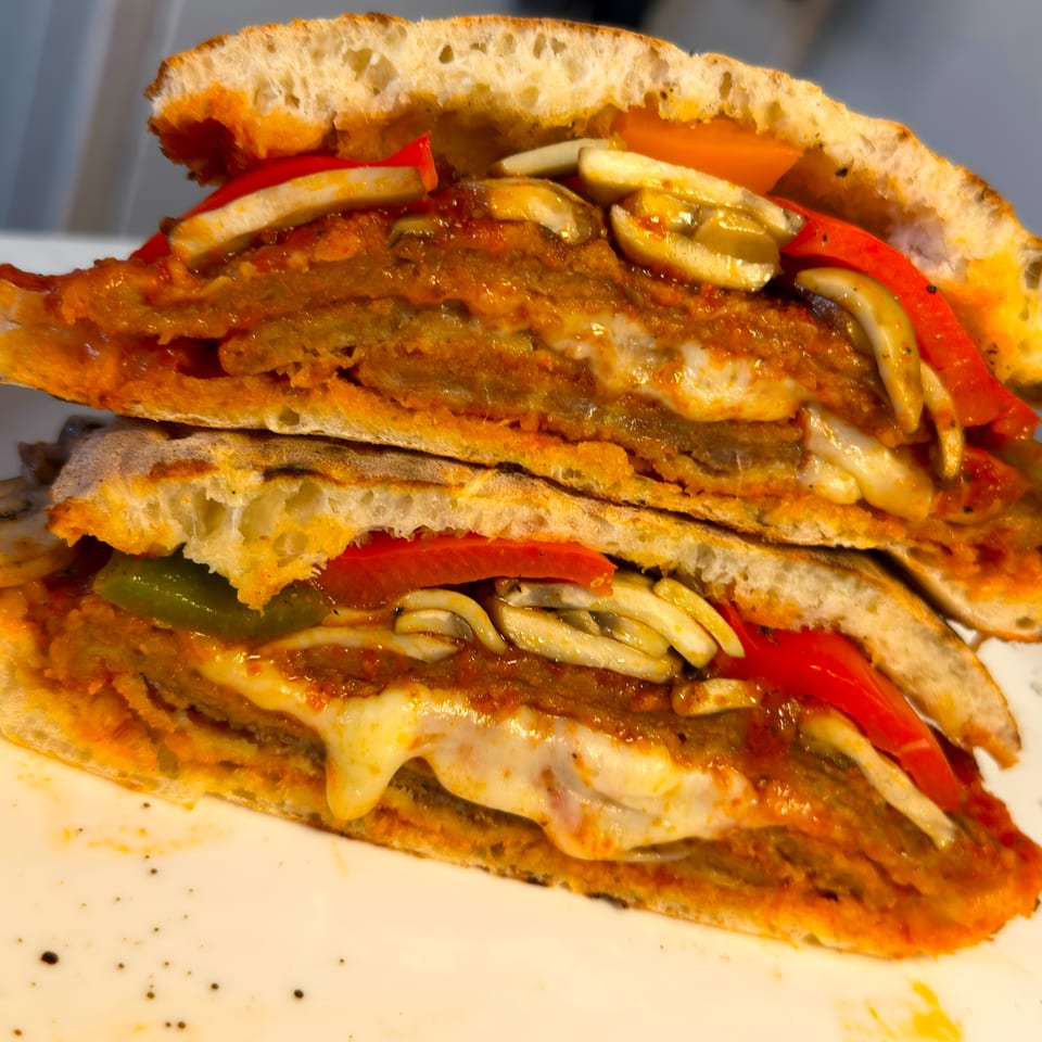Stacked toasted sandwiches filled with breaded cutlets, melted cheese, mushrooms, peppers, and tomato sauce on a plate.