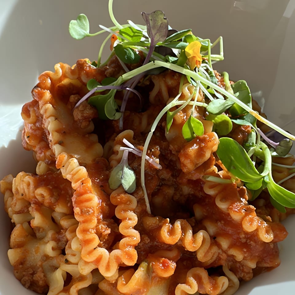 Bowl of ridged spiral pasta in tomato sauce, topped with microgreens and edible flowers.